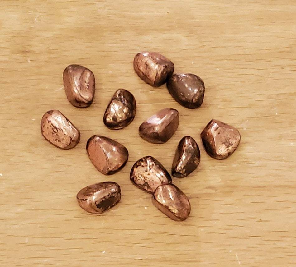 Solid copper tumbled pieces on a wooden surface, approximately 1 inch in size.