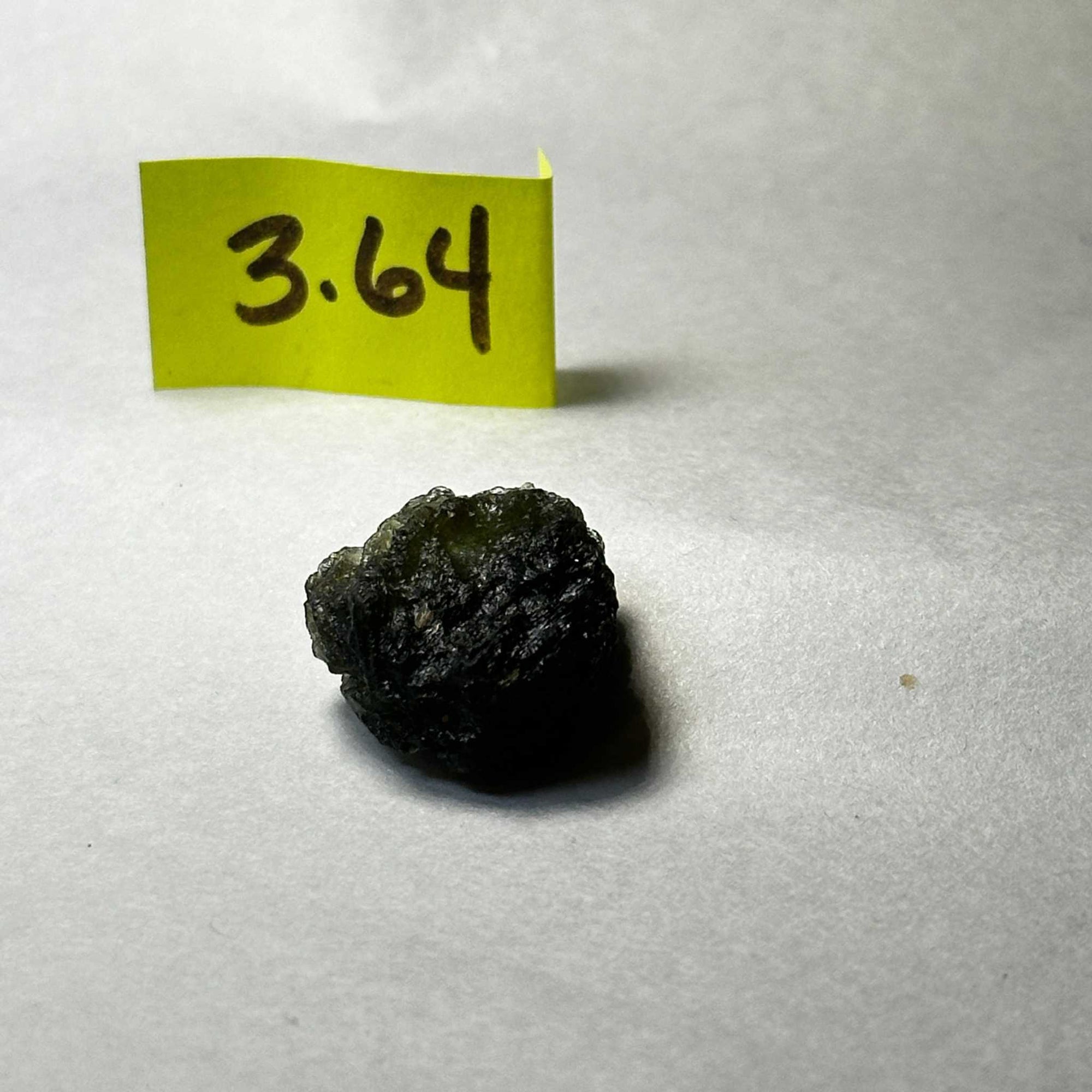 Raw Moldavite tektite stone weighing 3.64 grams on white background with yellow label