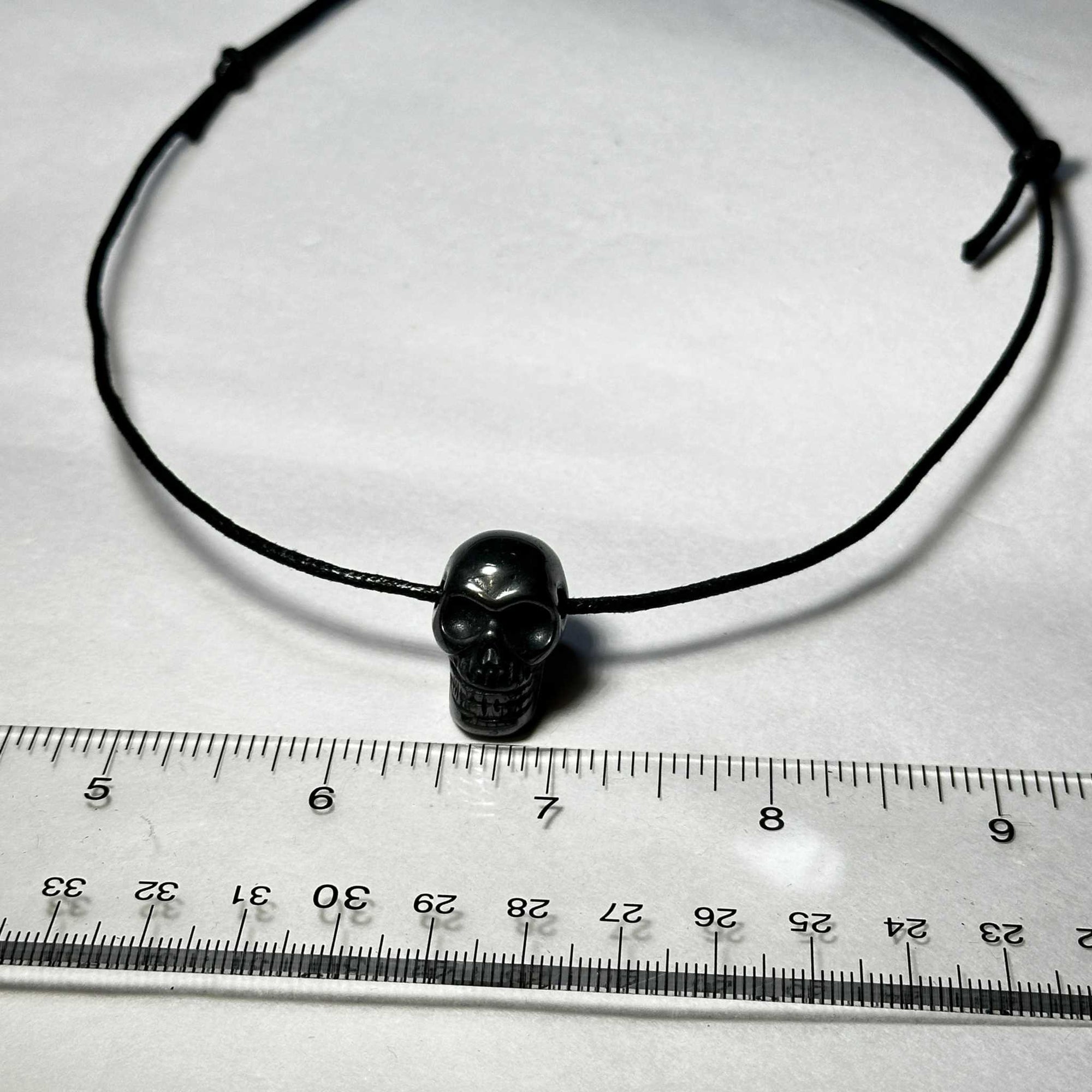 Hematite Skull Necklace on black slipknot cord with ruler for size reference.