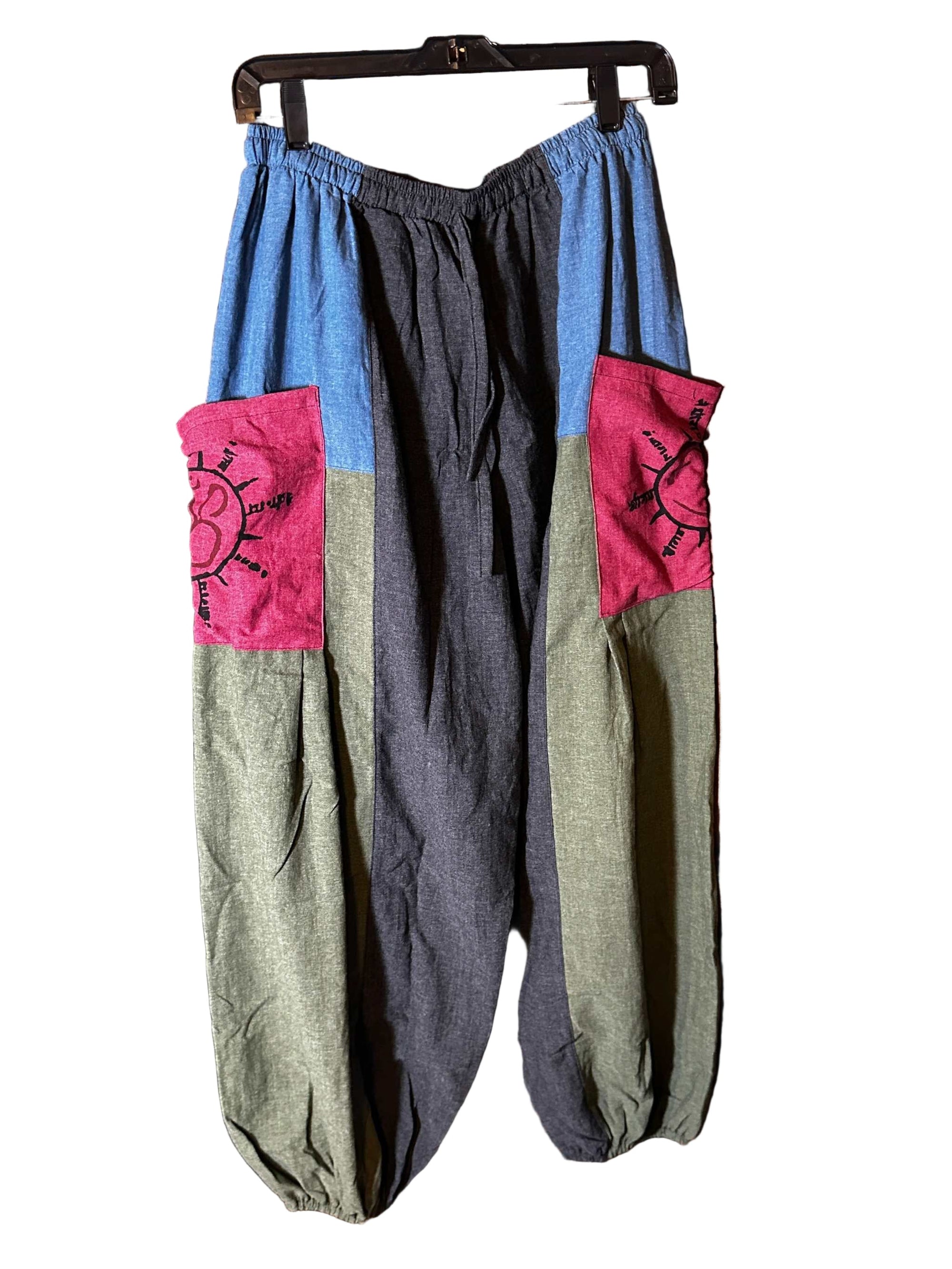 Handcrafted cotton Ohm pants with elastic waist and ankle cuffs, featuring assorted colorful patchwork and sun motif pockets.