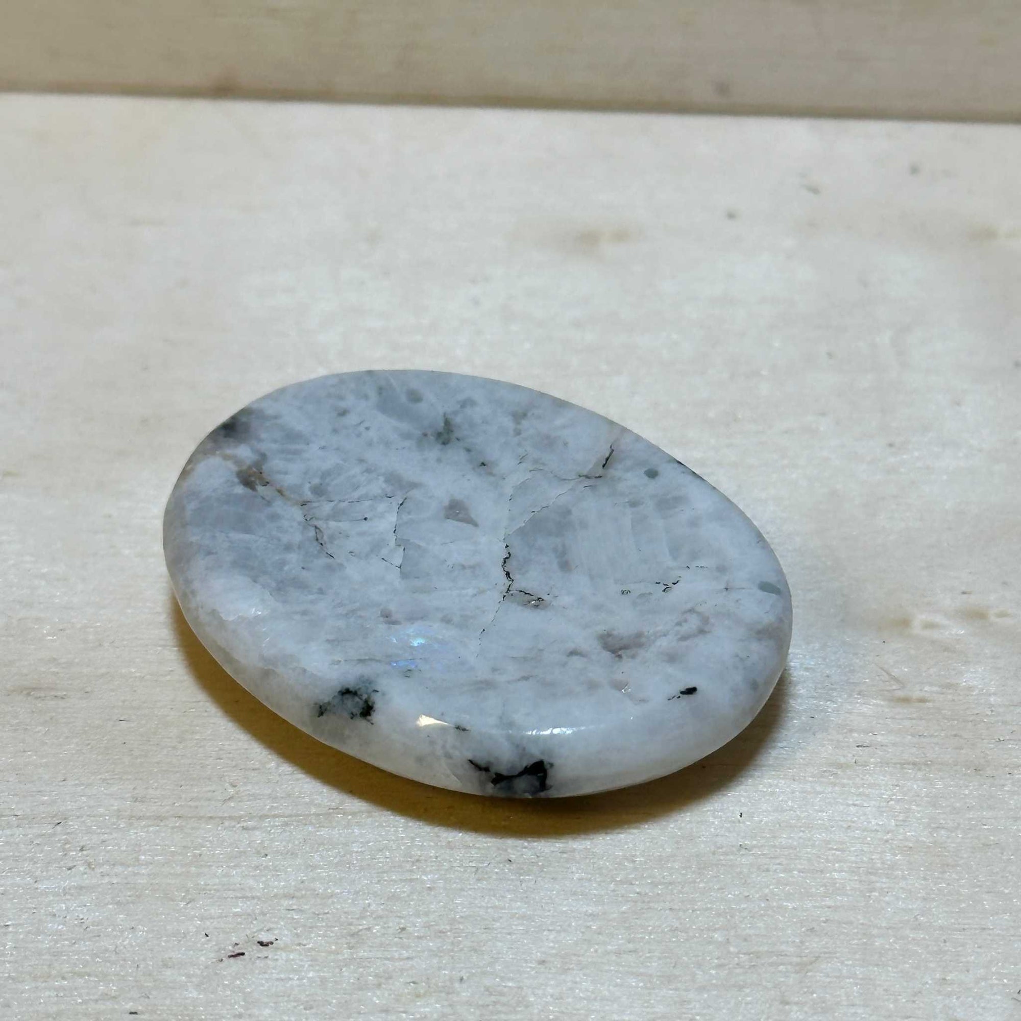 Rainbow Moonstone Comfort Stone with luminous adularescence on a wooden surface.