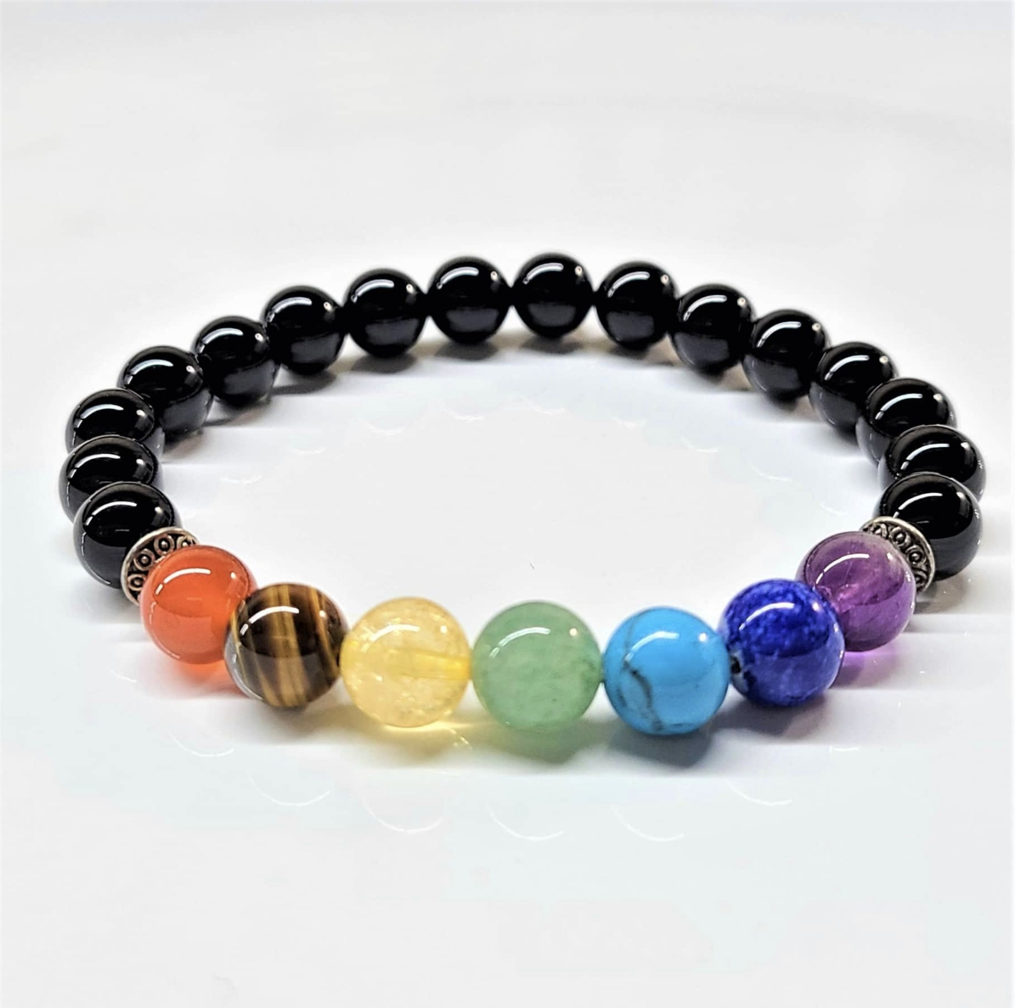 Black Onyx Chakra Bracelet with seven colorful chakra stones and round black onyx beads arranged in a circle on white background