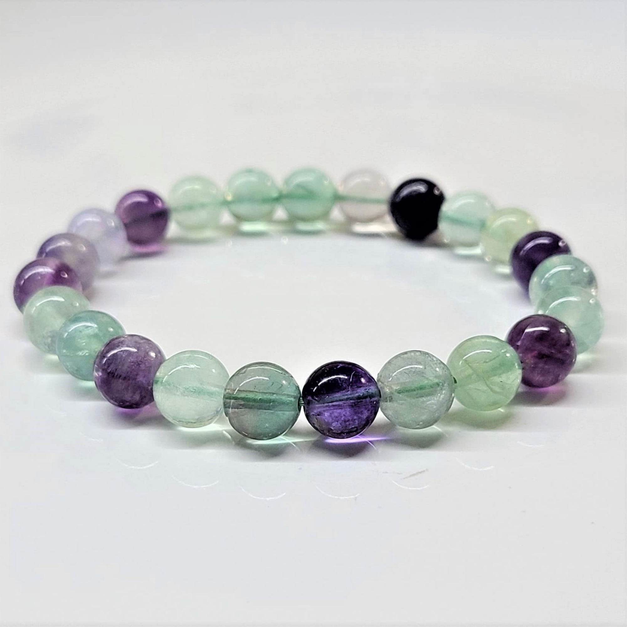 Fluorite round bead bracelet with multicolored stones in purple, green, and clear hues, ideal for stacking.