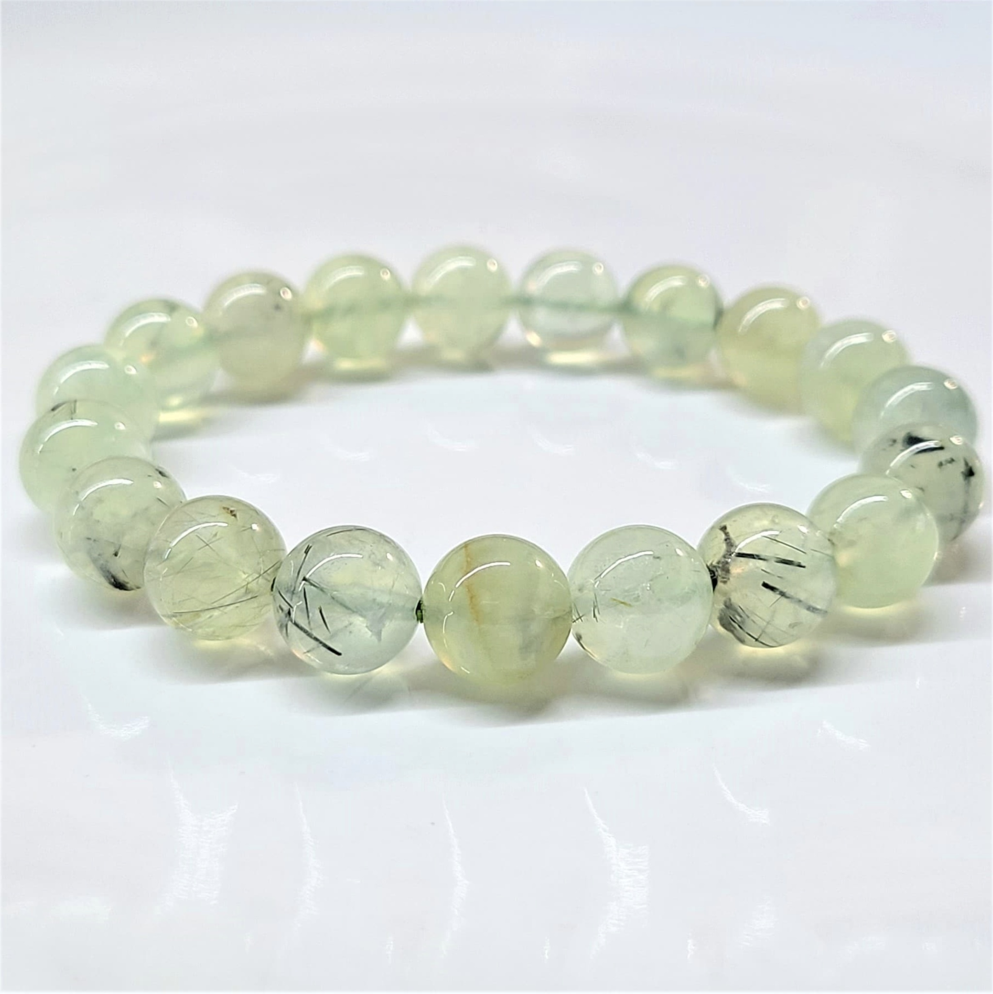 Prehnite stackable bracelet featuring round translucent light green beads with natural black inclusions for calming and protective energy