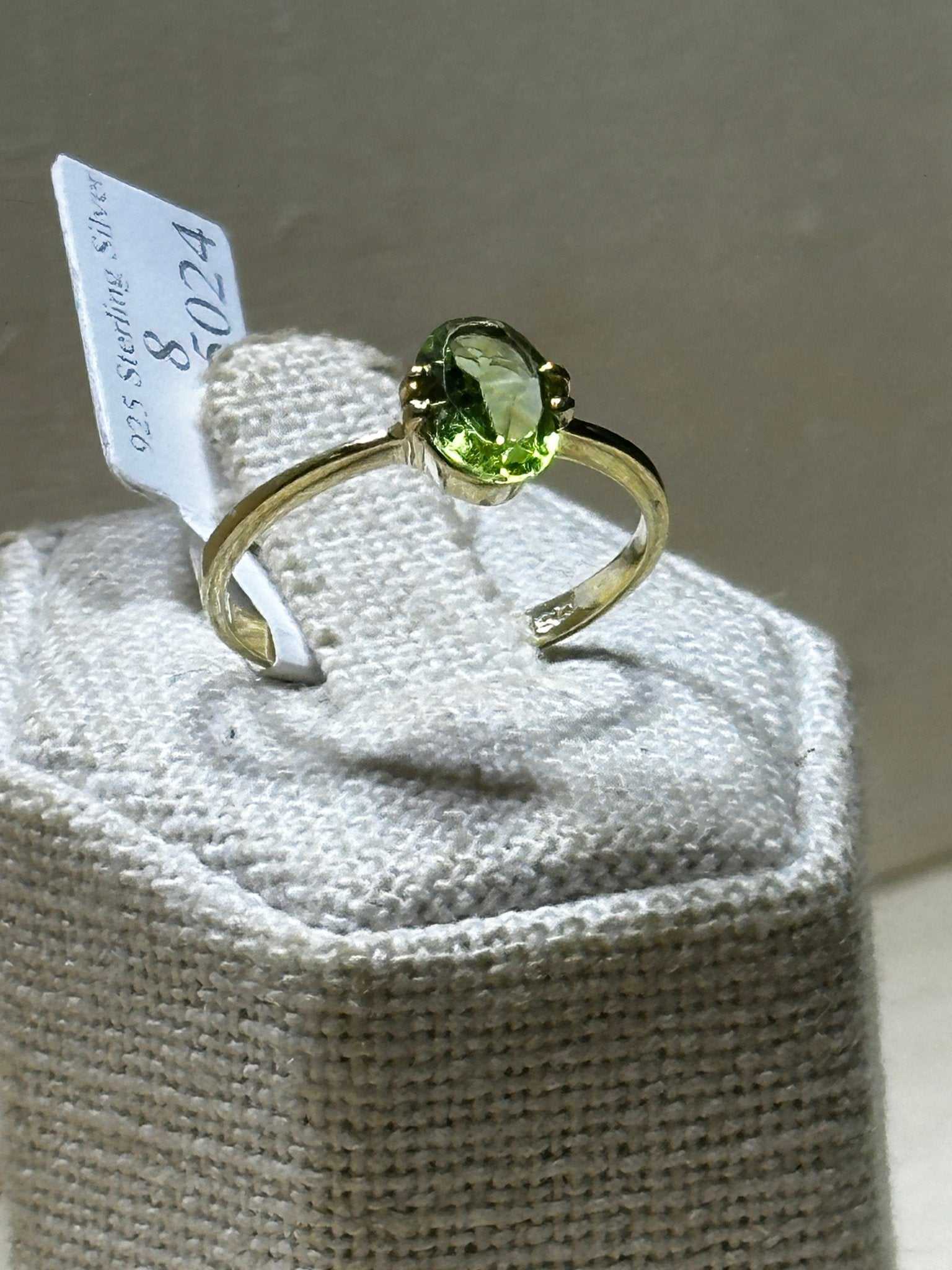 Peridot ring size 8 with oval green gemstone set in sterling silver band displayed on textured cushion