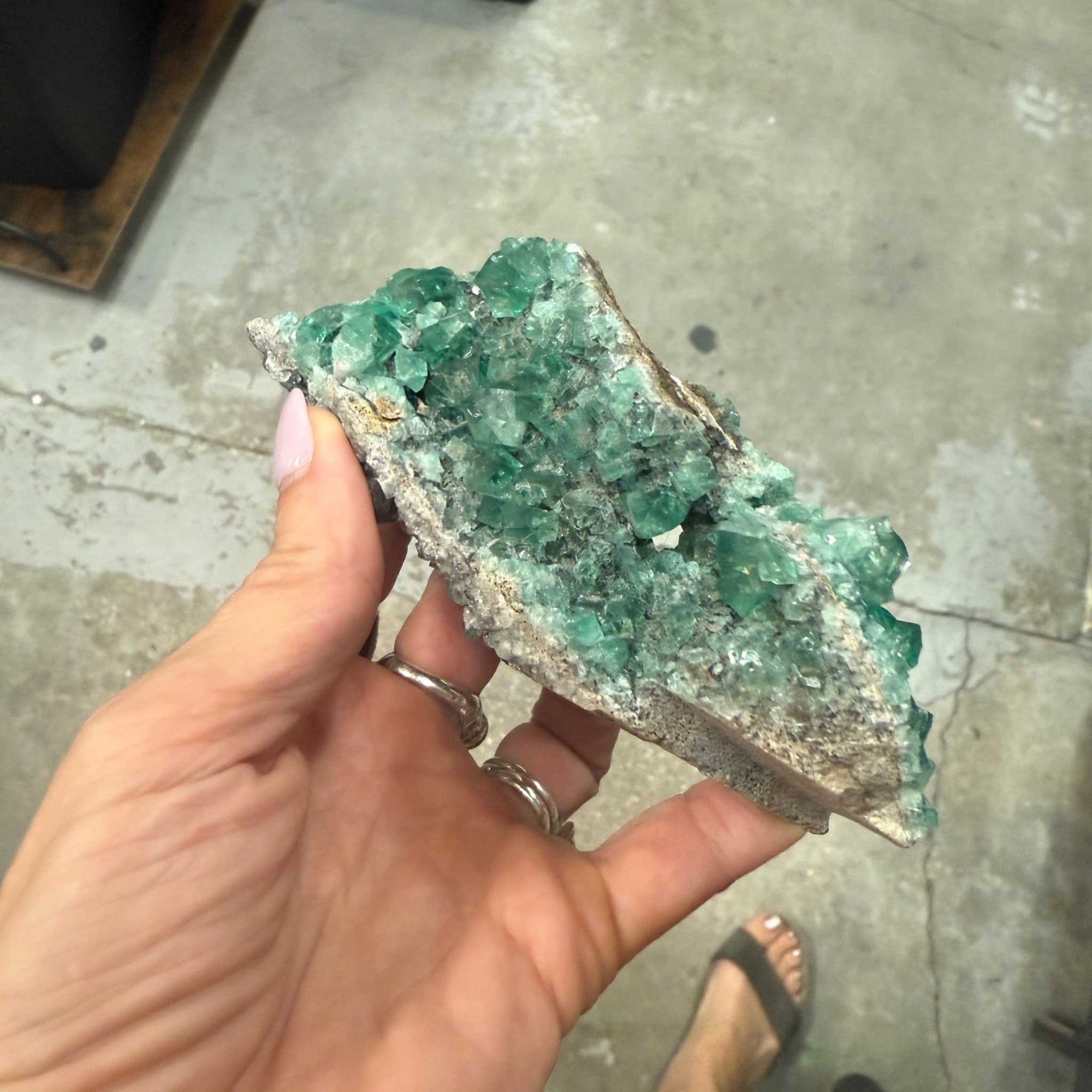 Hand holding a 6-inch green fluorite specimen known as the River of Intuition with vibrant green crystal formations on a stone base