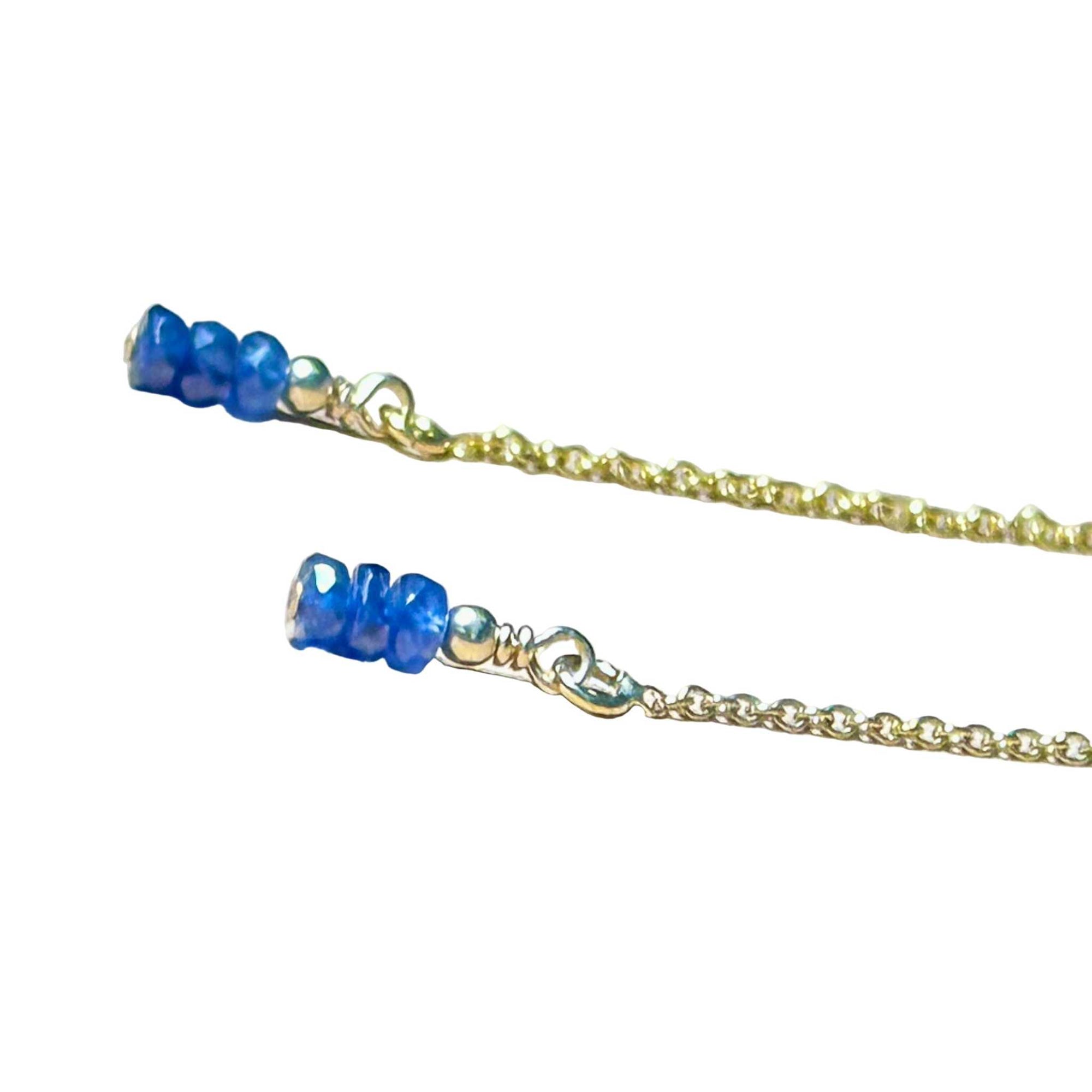 Gold chain earrings with blue Sapphire beads on a background.