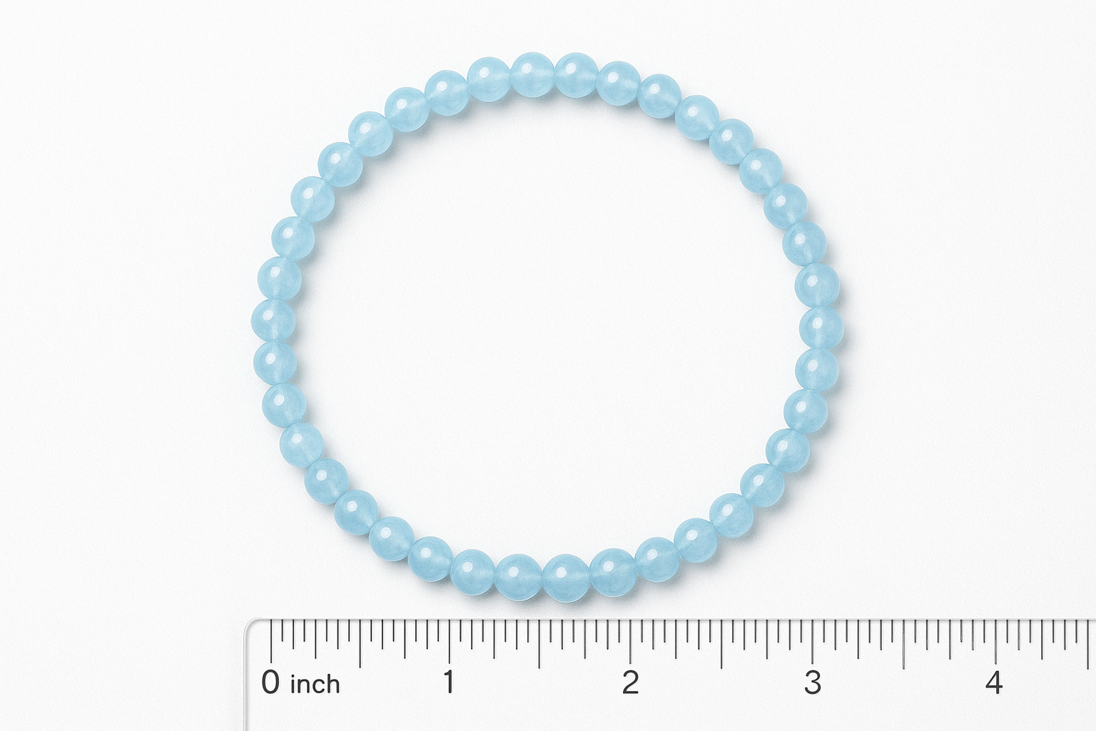 Create a realistic digital photo of a light blue aquamarine elastic beaded bracelet made of 4mm round polished beads. The bracelet has exactly 42 beads and is laid flat in a perfect circle on a white background. Include a clear inch ruler scale grid below and to the left of the bracelet for size reference. The inner diameter should be approximately 2.25 inches. The lighting should be bright and even, like a professional product image for Amazon, showing the gentle shine of the beads and accurate scale.