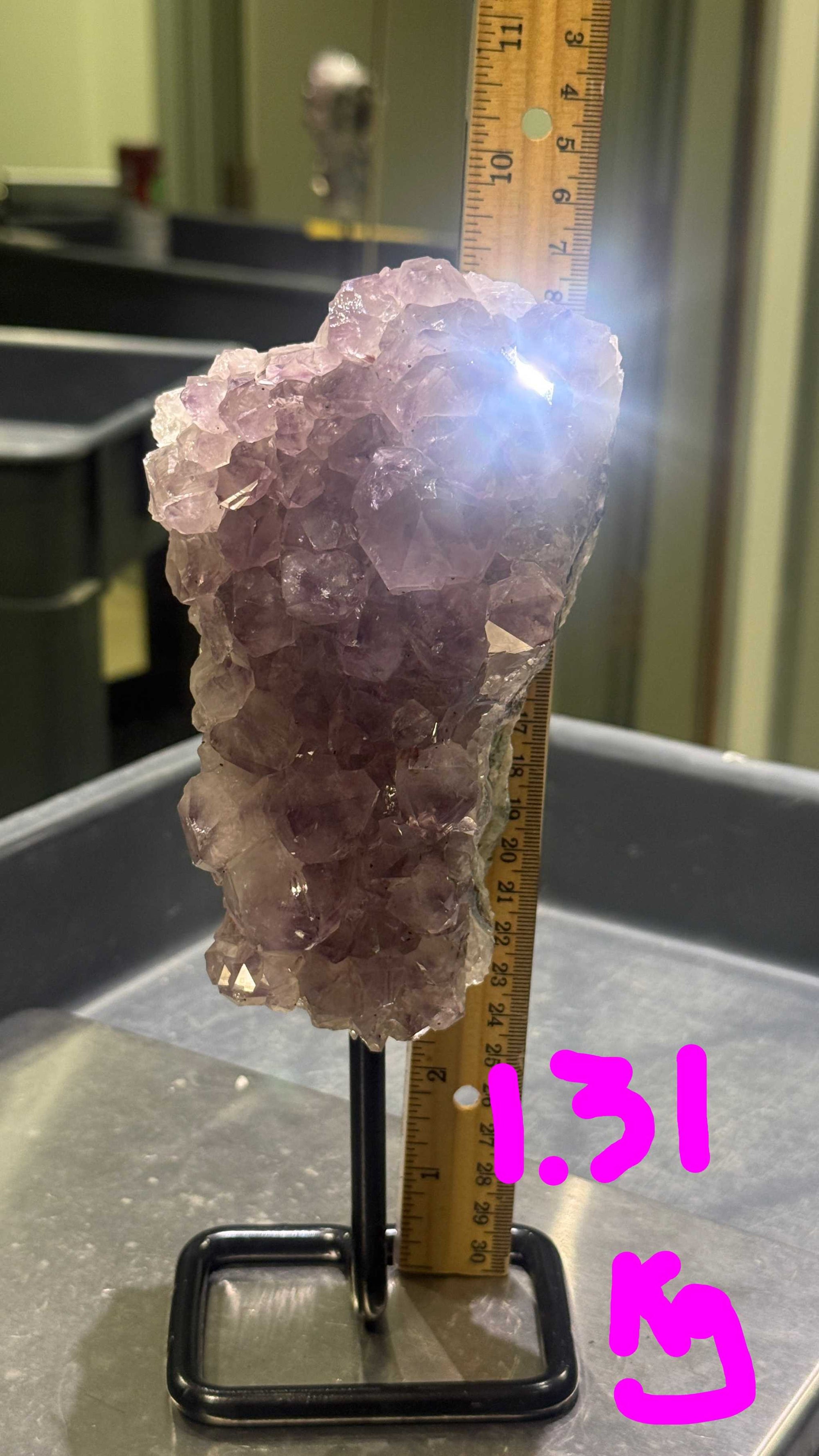 Amethyst crystal cluster on a stand with a ruler for scale