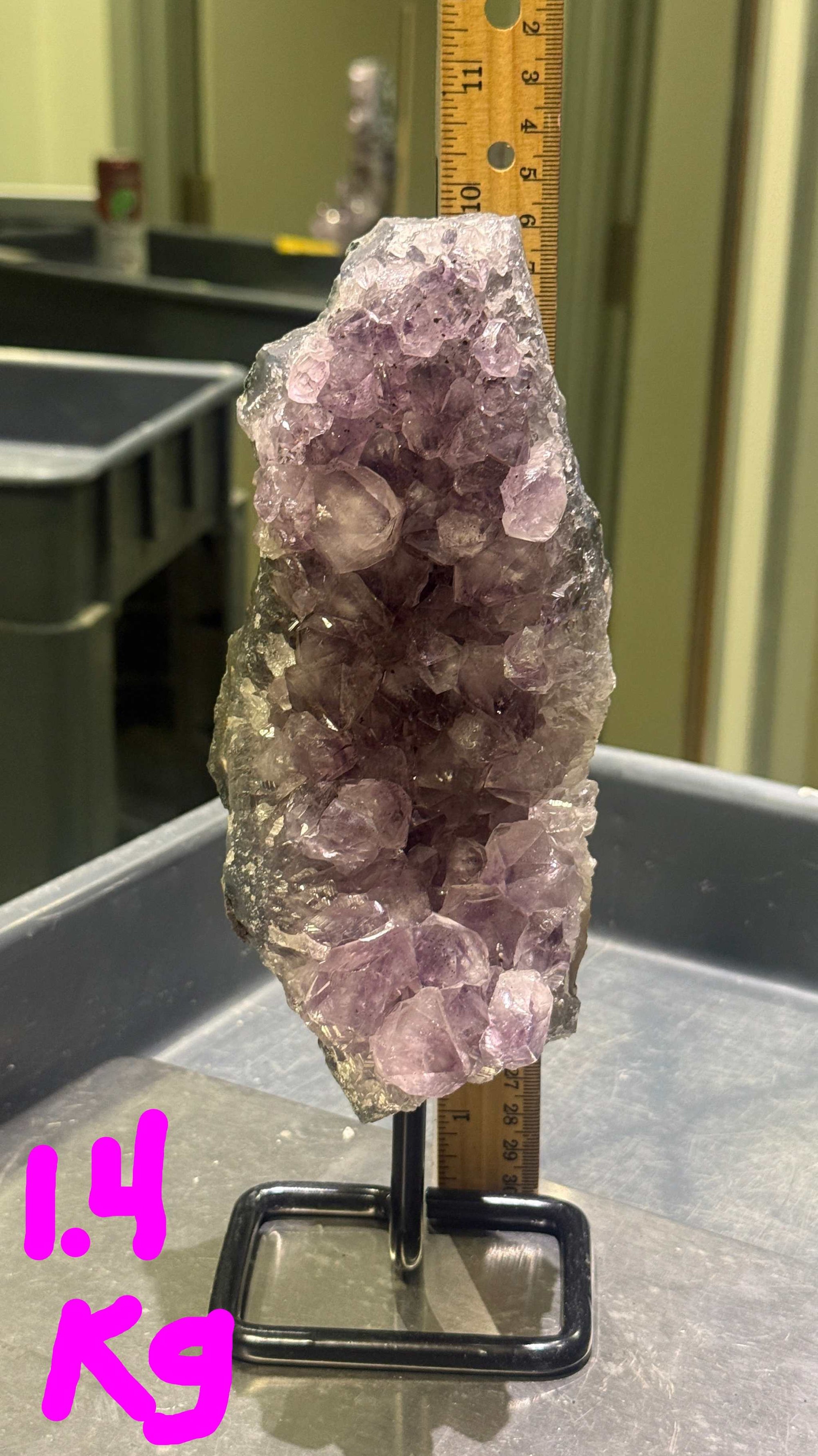 Amethyst crystal on a stand with a ruler for scale in an indoor setting