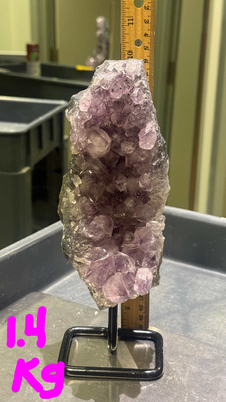 Amethyst crystal on a stand with a ruler for scale in an indoor setting