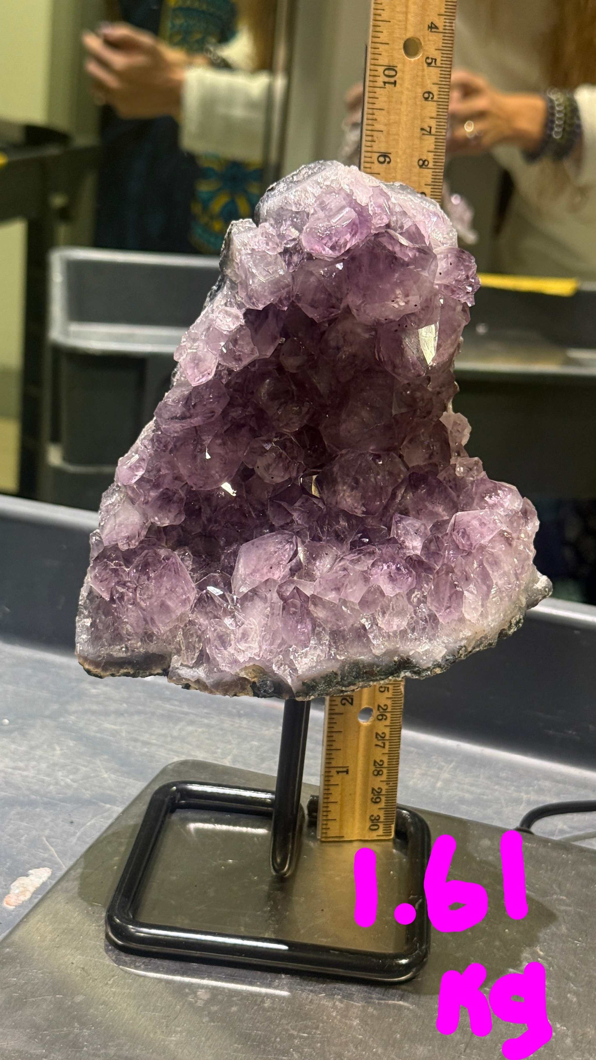 Amethyst crystal on a stand with a ruler for scale, placed on a reflective surface.