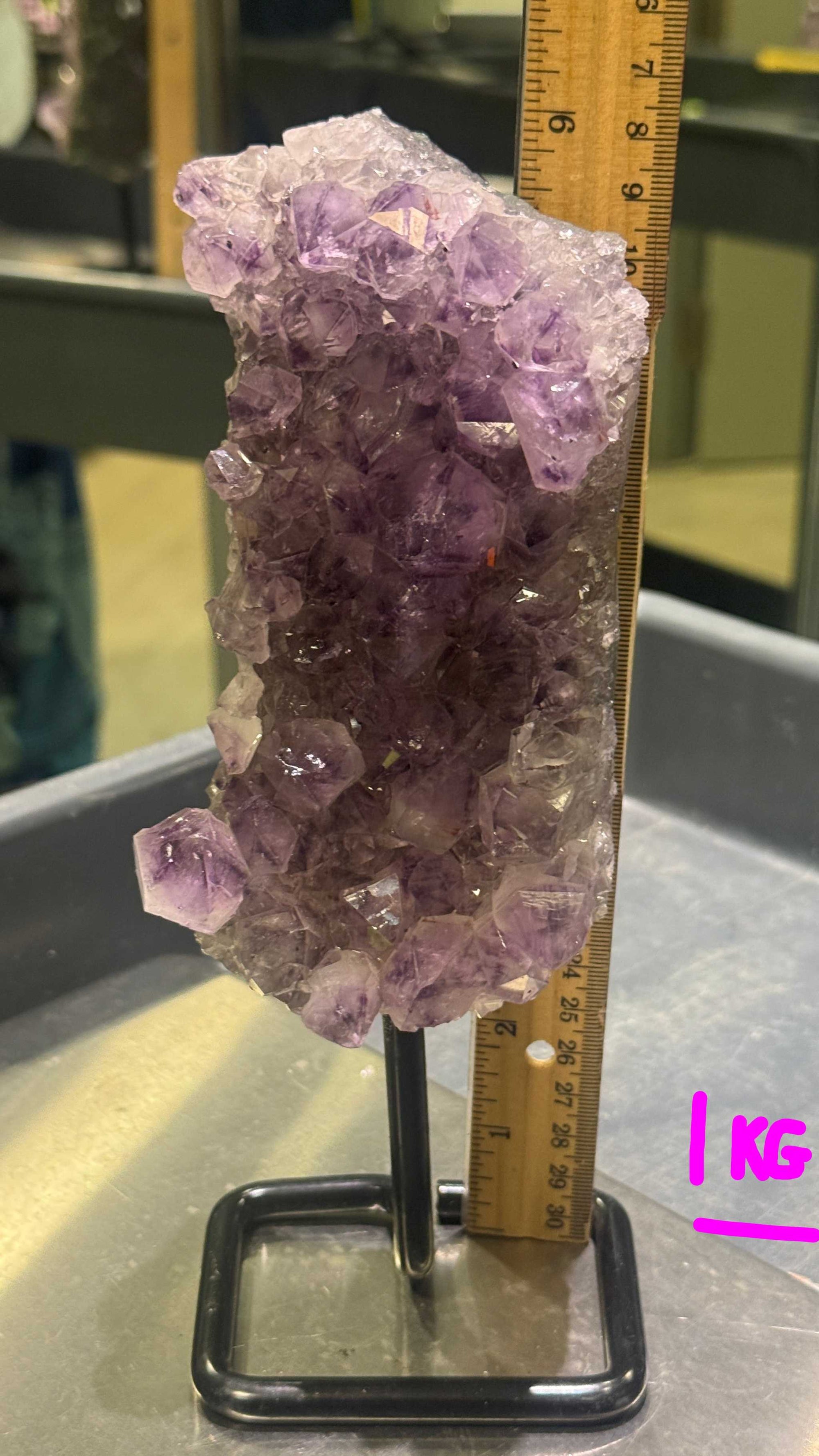 Amethyst crystal cluster on a stand with a ruler for scale.