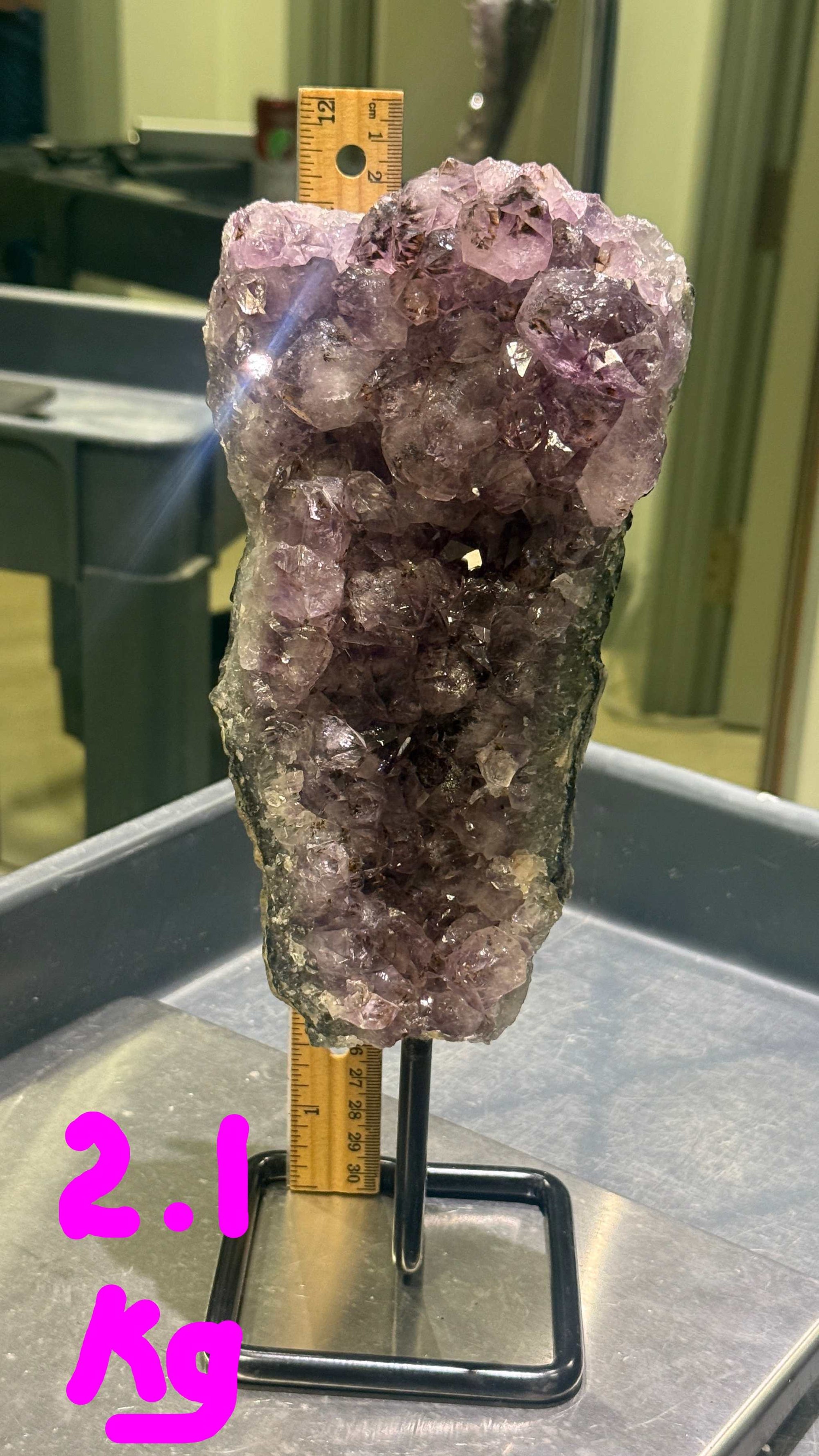 Amethyst crystal cluster on a stand with a ruler for scale in an indoor setting