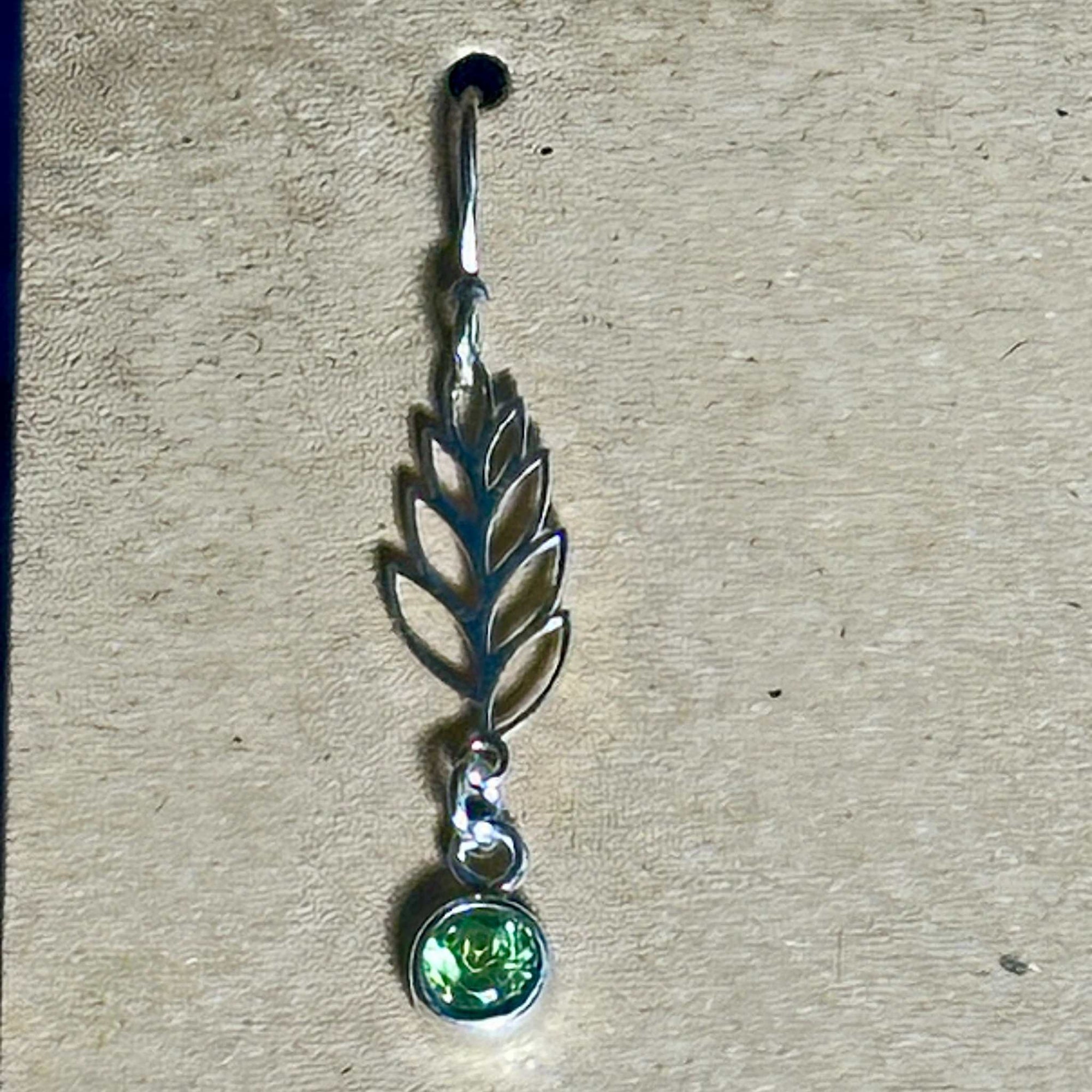 Silver leaf-shaped earring with a green Peridot gemstone on a beige background