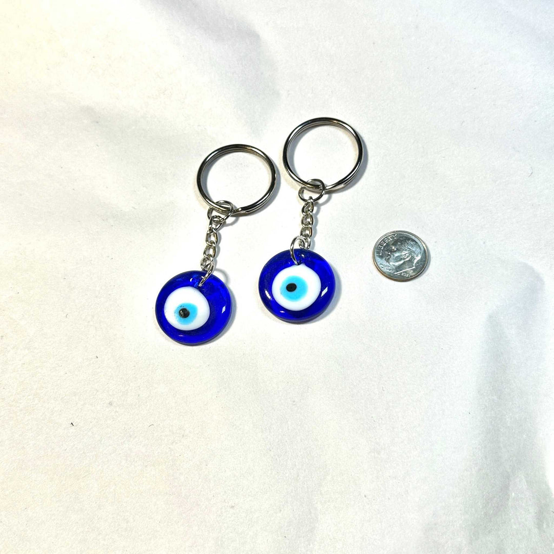Two blue Evil Eye small keychains with silver key rings displayed next to a quarter coin for size comparison