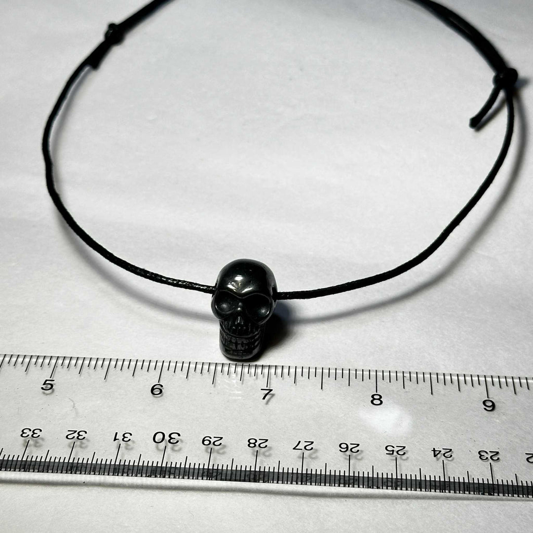 Hematite Skull Necklace on black slipknot cord with ruler for size reference.