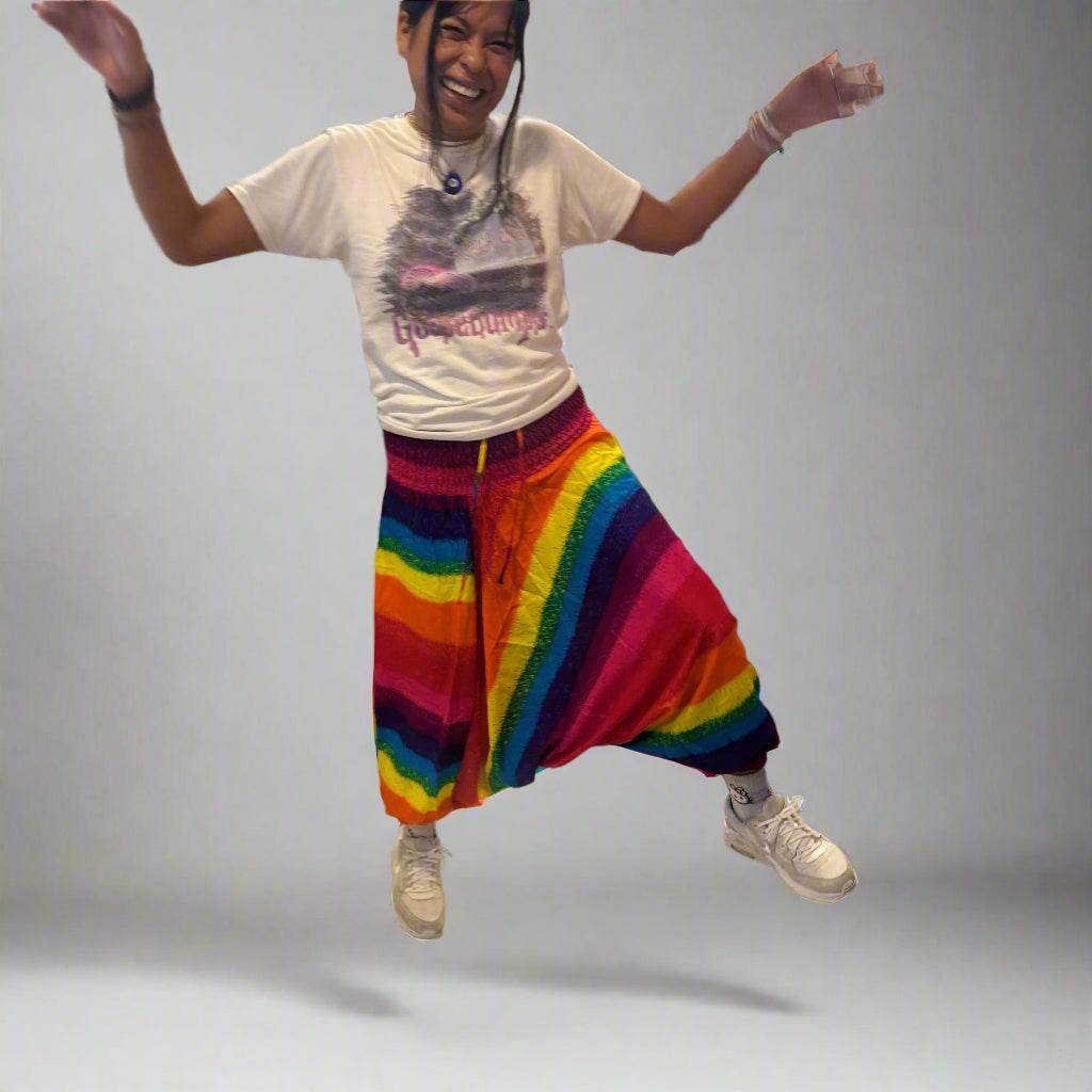 Person jumping wearing colorful rainbow harem Alibaba onesie pants with white t-shirt and sneakers