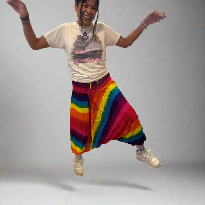 Person jumping wearing colorful rainbow harem Alibaba onesie pants with white t-shirt and sneakers