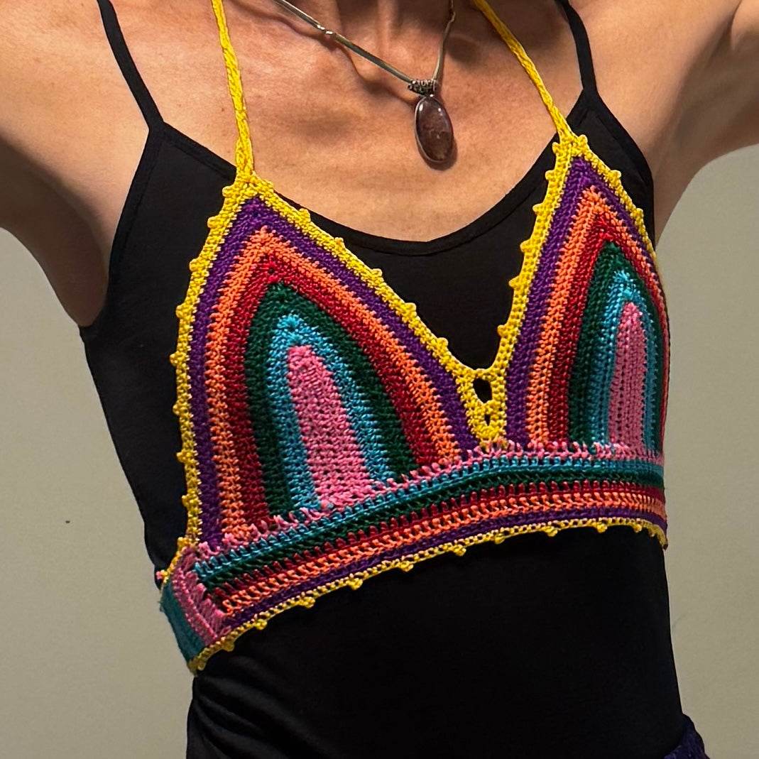Colorful handmade crochet rainbow bikini top worn over black tank top with yellow straps