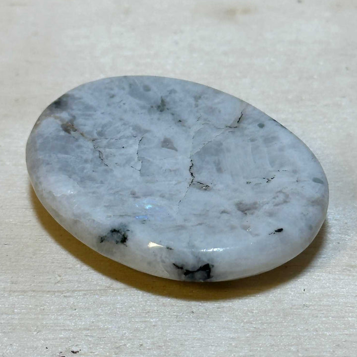 Rainbow Moonstone Comfort Stone with luminous adularescence on a wooden surface.