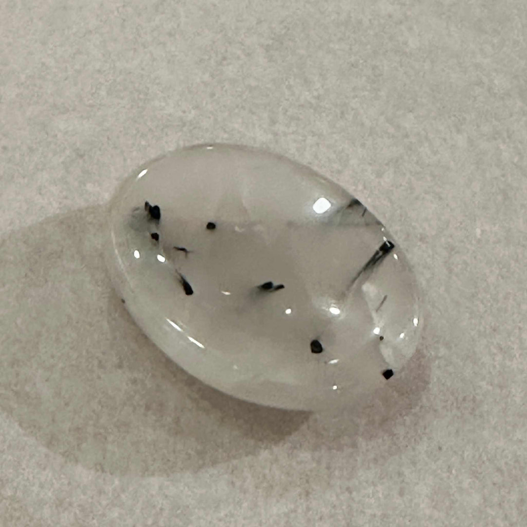 Polished rutilated quartz comfort stone with needle-like inclusions on a gray surface