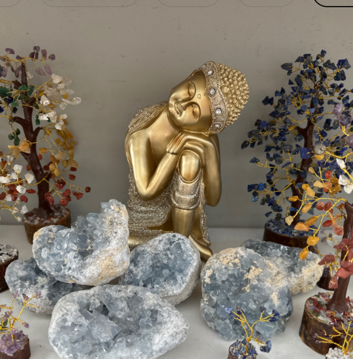 Celestite Cosmic Craters displayed with decorative trees and a gold Buddha statue.
