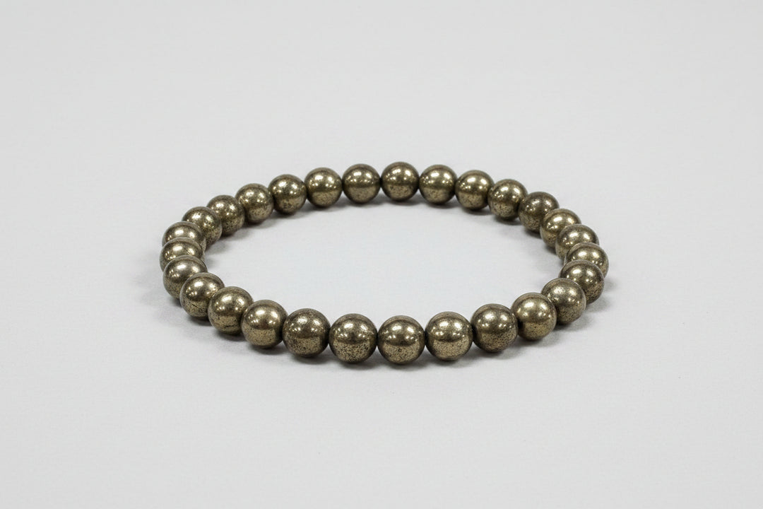 Pyrite beaded bracelet on a white surface with a blurred floral background