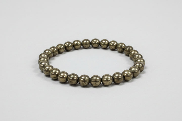 Pyrite beaded bracelet on a white surface with a blurred floral background