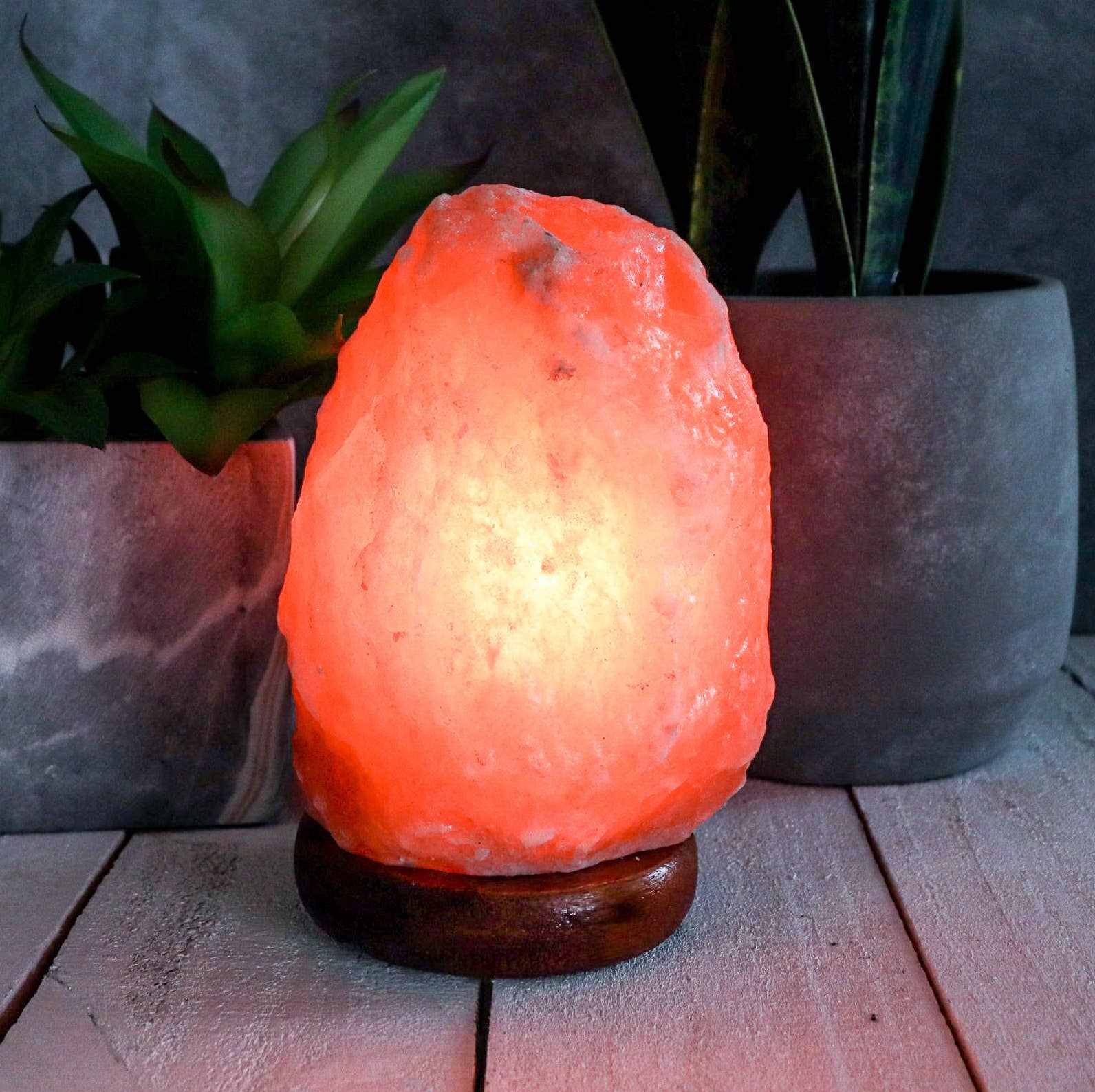 Natural pink Himalayan salt lamp glowing softly on wooden base with plants in background