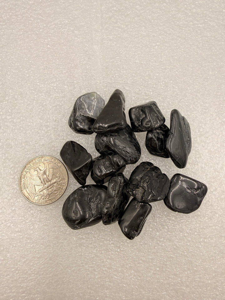 Black tourmaline tumbled stones with a quarter for scale