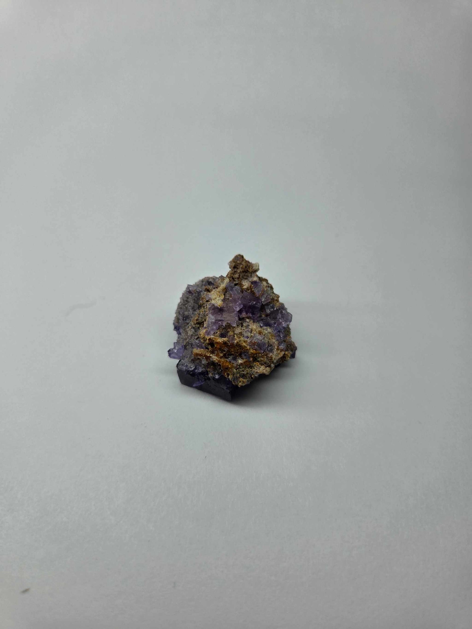 Small purple fluorite specimen cluster growing through matrix on gray background