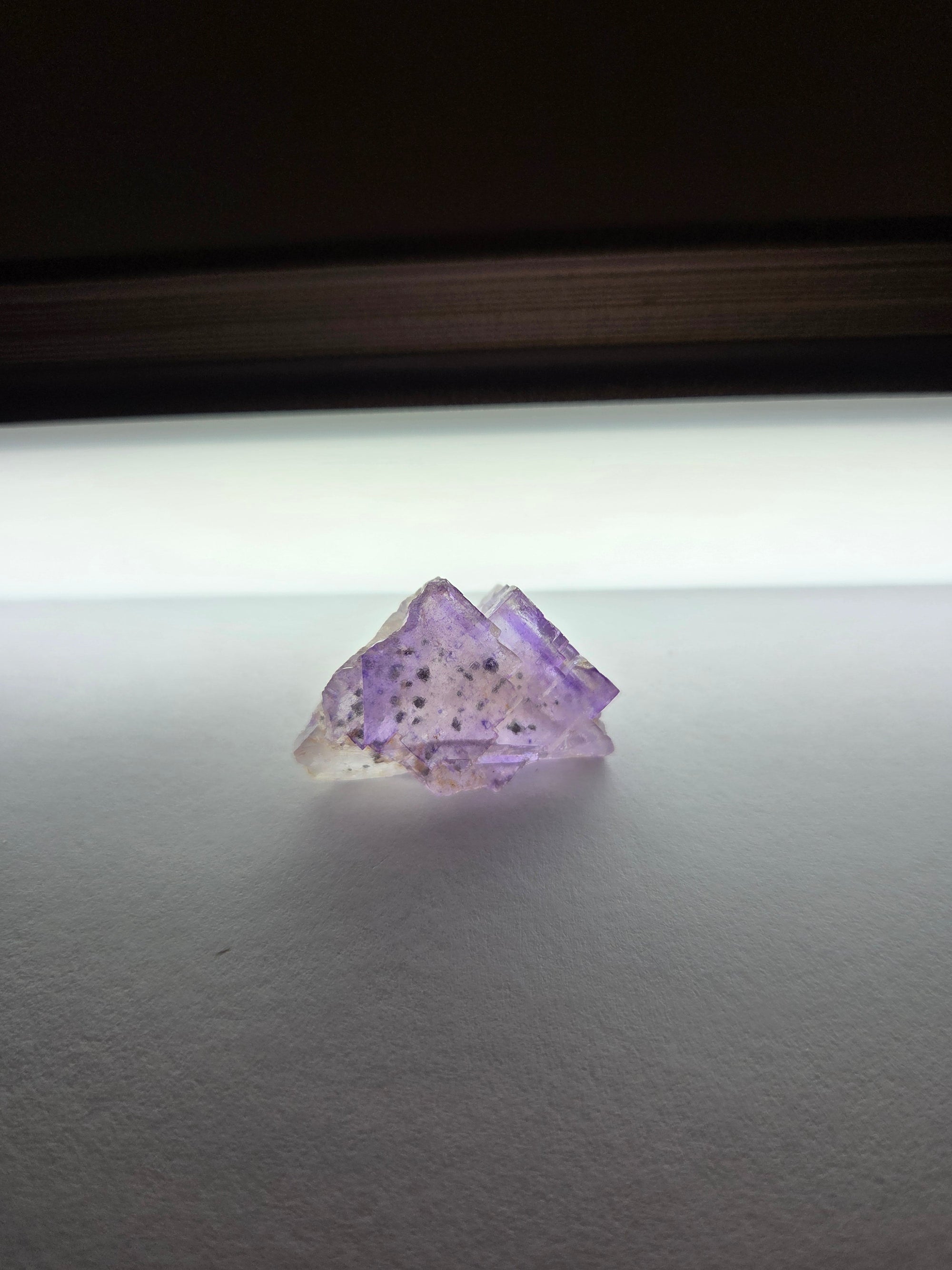 Small Purple Fluorite specimen with speckled violet window on white surface