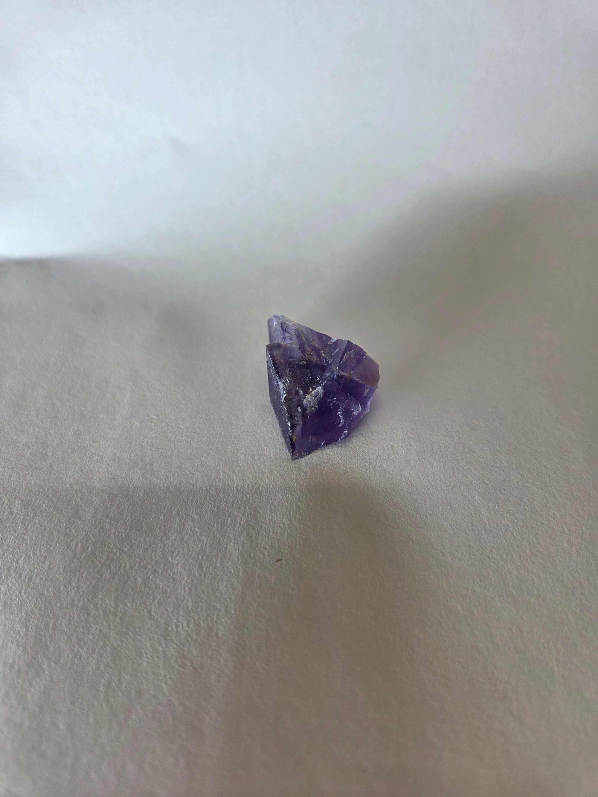 Small purple fluorite crystal specimen with stepped cubic geometry on a plain background