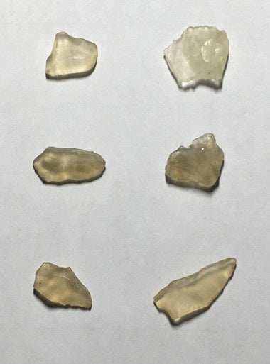 Libyan Desert Glass Tektite, less than 1 gram, unique yellowish fragments on white background.